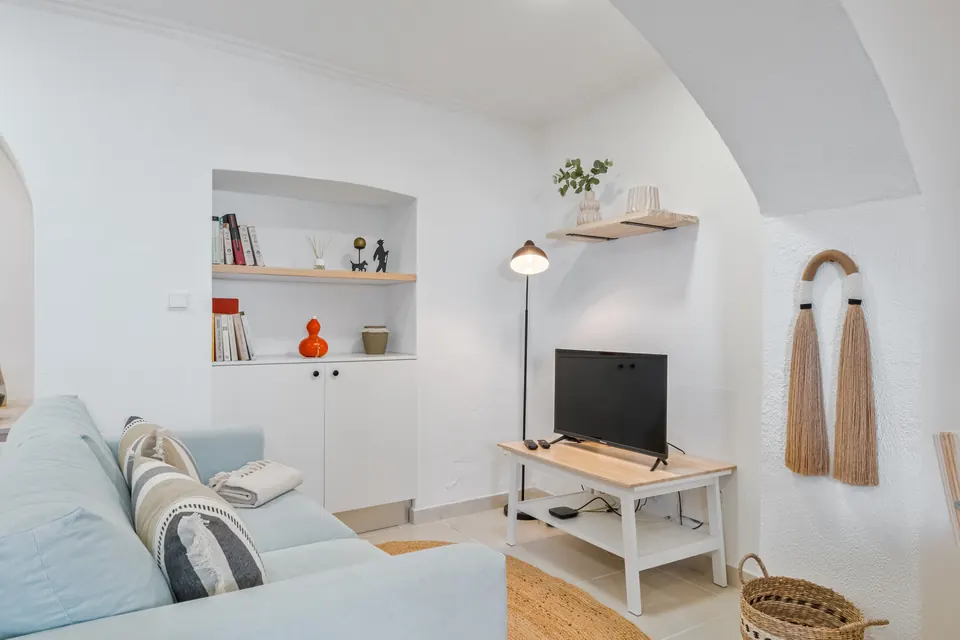 Sala de estar com sofá azul-claro, televisão e estante embutida na parede caiada